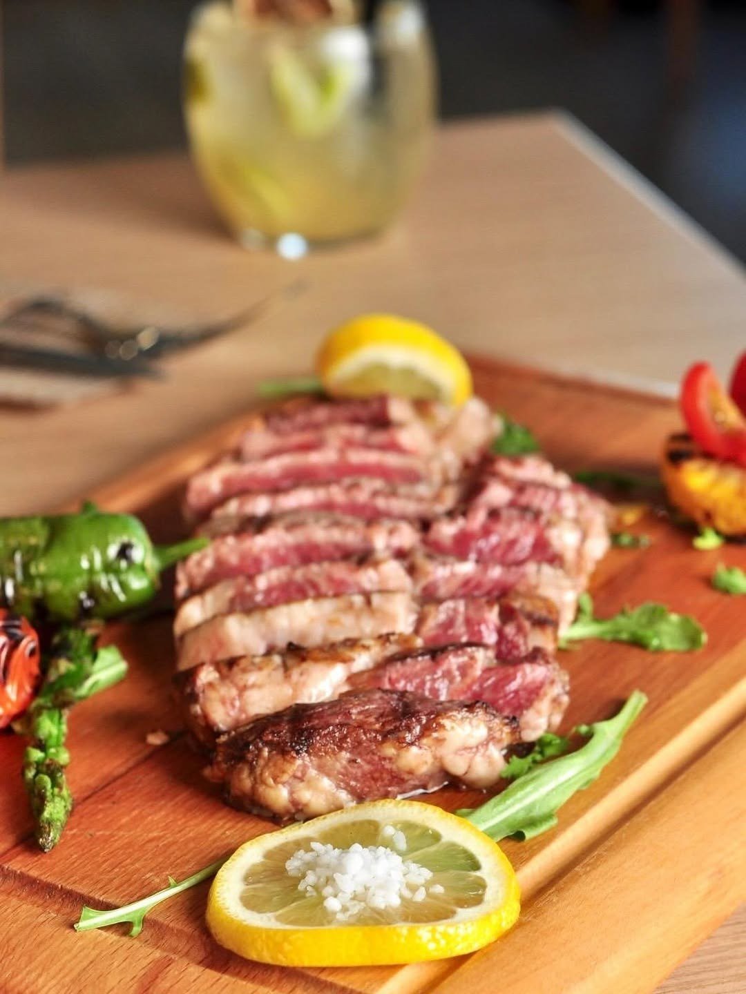 Ribeye grelhado fatiado numa tábua, com limão e pimentos