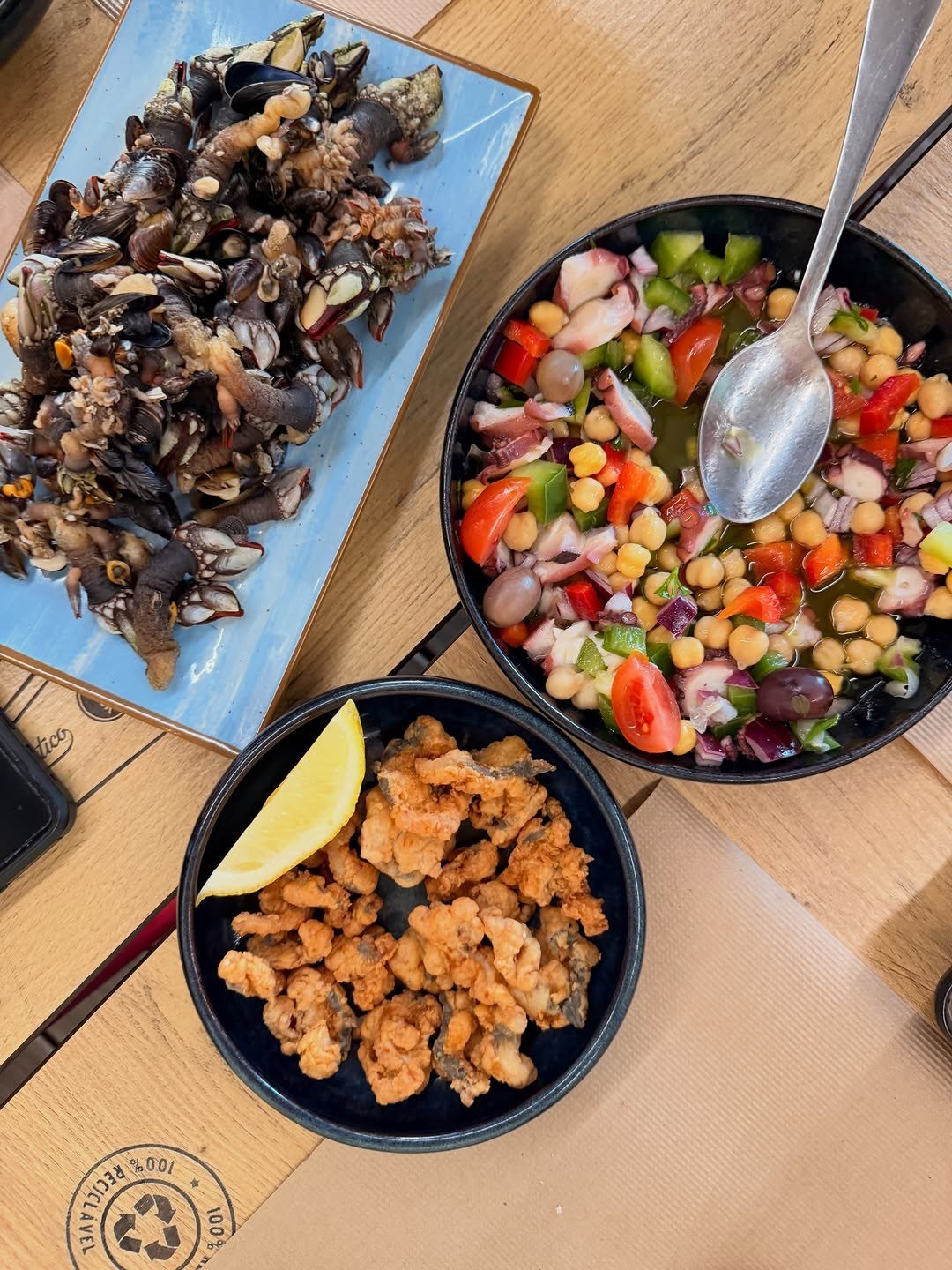 Percebes, salada de grão com legumes e uma taça de fritos com limão, vistos de cima